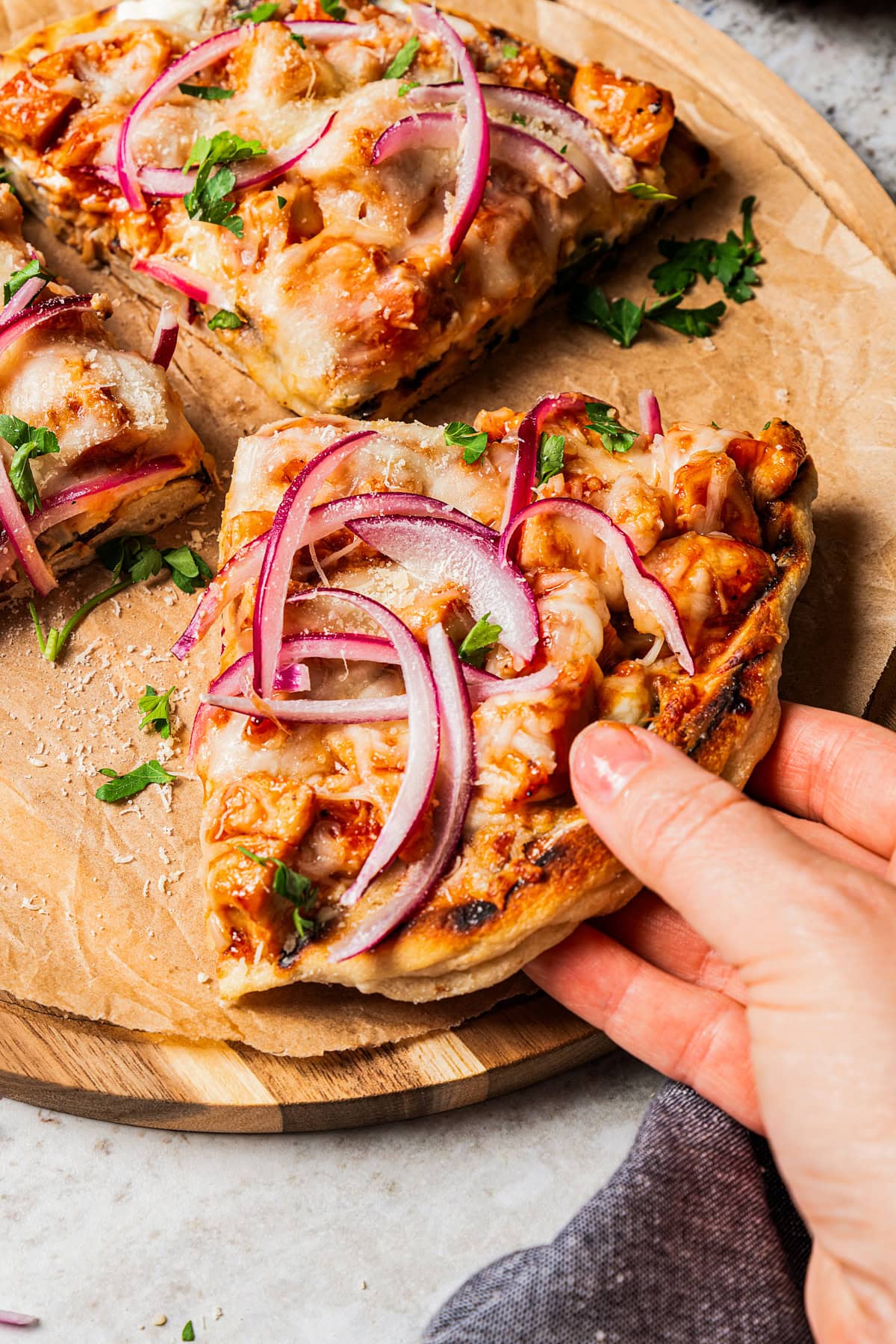 A hand picking up a pizza slice topped with barbecue chicken and sliced red onions.