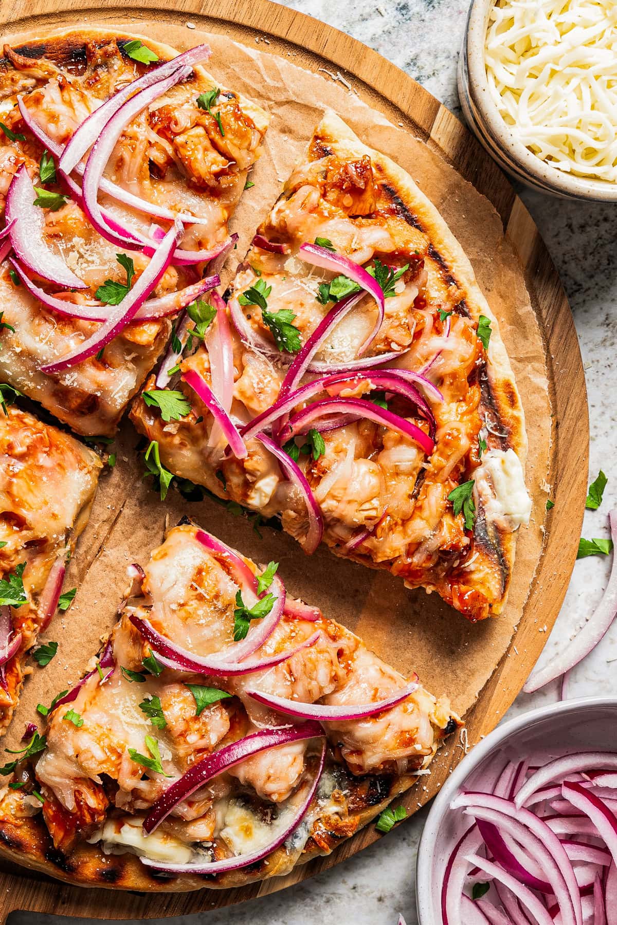 Pizza is served on a wooden board and cut up into slices.