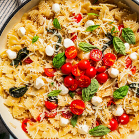 A pot of bow-tie pasta topped with cherry tomatoes, basil leaves, and fresh mozzarella balls.