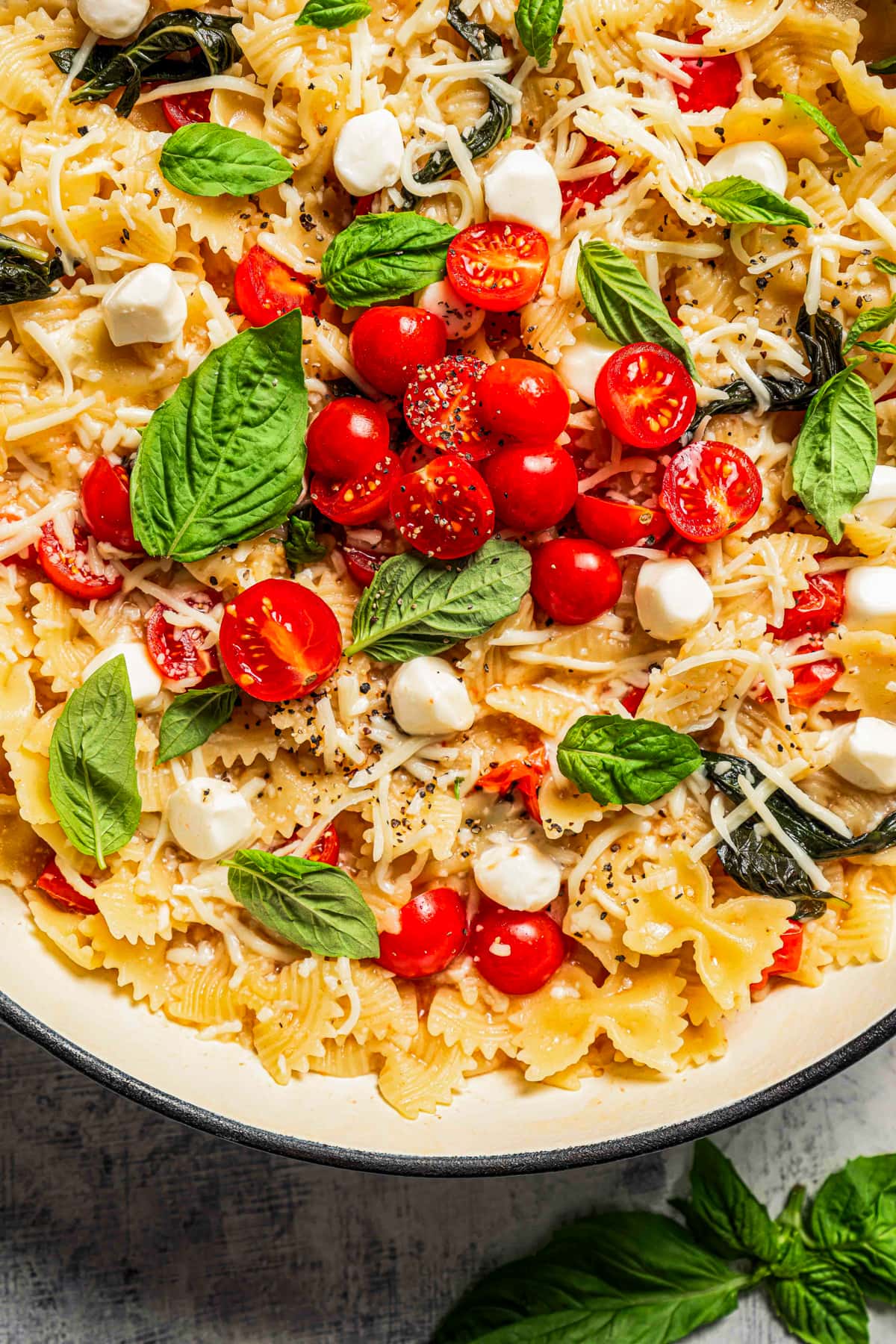 Close-up photo of pasta mixed with tomatoes, cheese balls, and basil leaves.