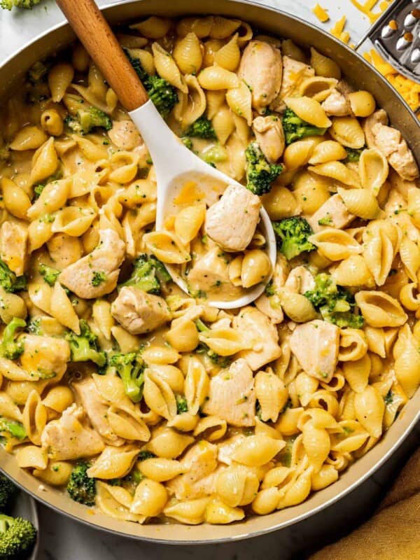 Close up overhead photo of a large skillet full of chicken and broccoli pasta with a slotted spoon.