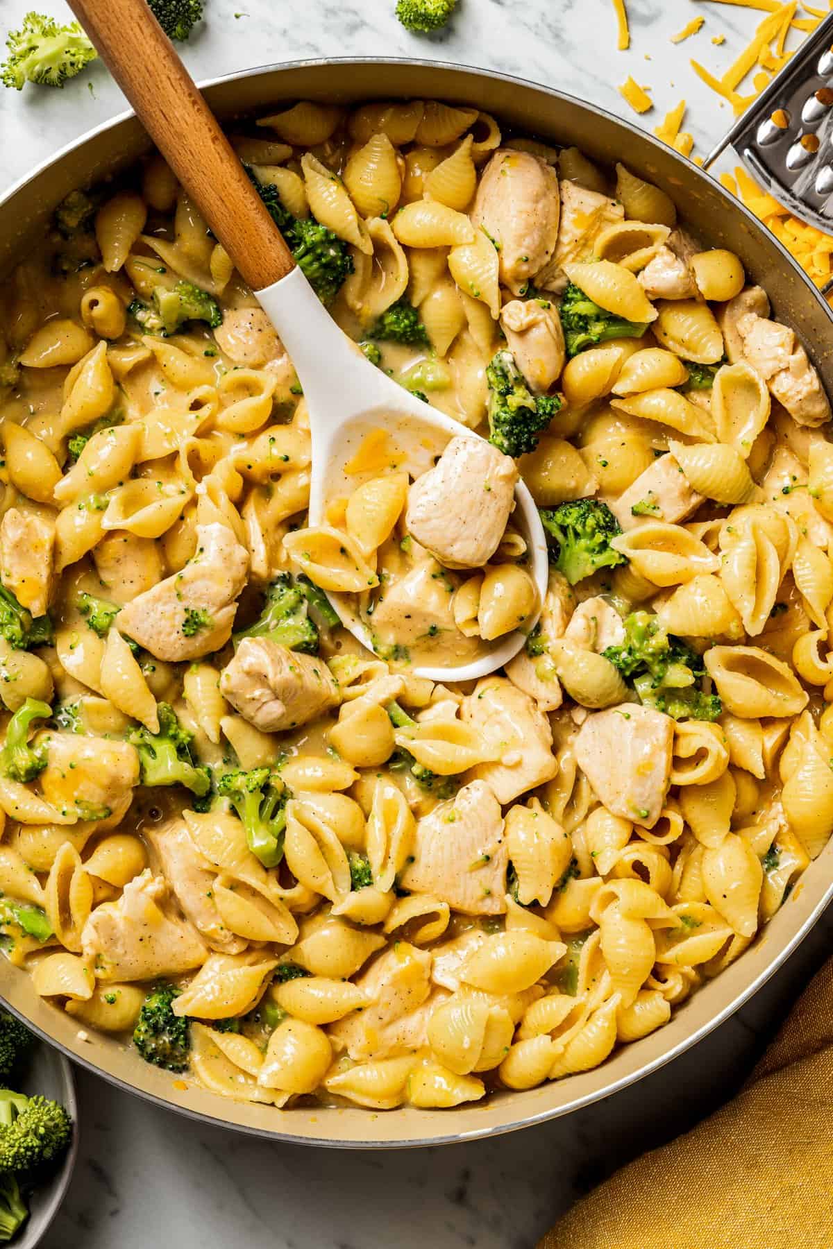 Close up overhead photo of a large skillet full of chicken and broccoli pasta with a slotted spoon.