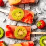 Four kiwi strawberry fruit popsicles surrounded by sliced kiwis and strawberries.
