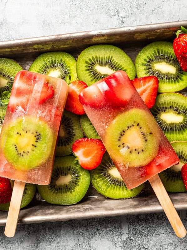Two homemade fruit popsicles with strawberries and kiwis on a metal tray.
