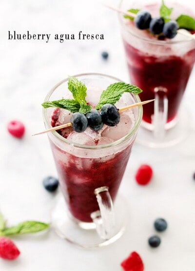 A colorful Agua Fresca drink in a tall glass with blueberries and mint
