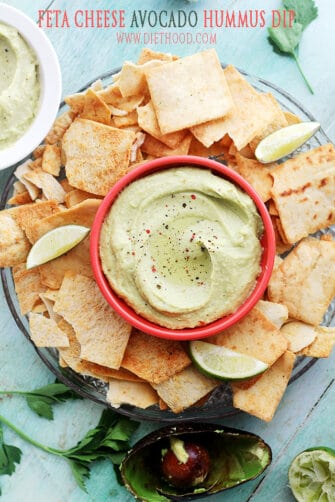 A platter of pita chips with a red bowl of avocado hummus in the middle