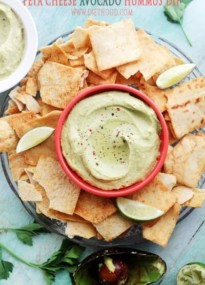 A platter of pita chips with a red bowl of avocado hummus in the middle