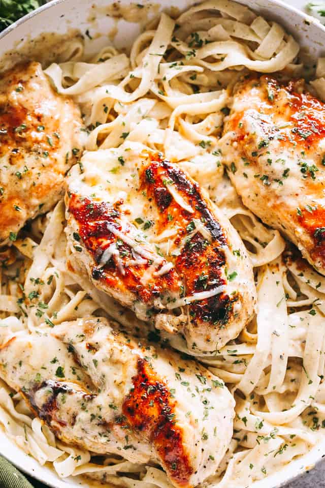 Close up overhead view of fettuccine alfredo in a skillet topped with baked chicken breasts.