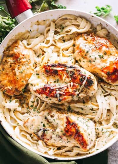 Overhead view of fettuccine alfredo in a skillet topped with baked chicken breasts.