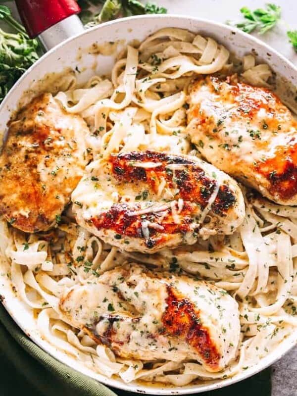 Overhead view of fettuccine alfredo in a skillet topped with baked chicken breasts.