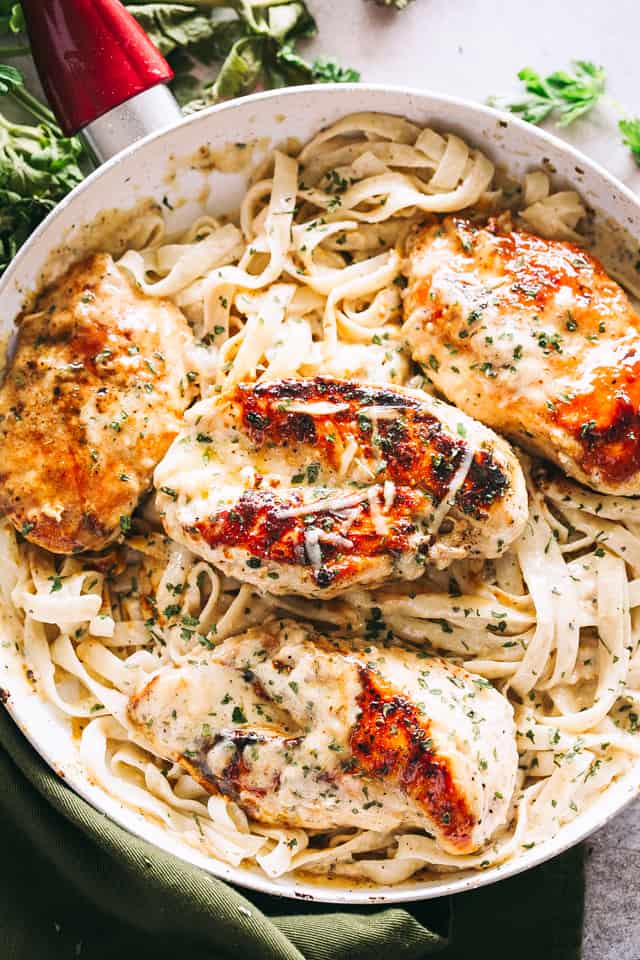 Overhead view of fettuccine alfredo in a skillet topped with baked chicken breasts.