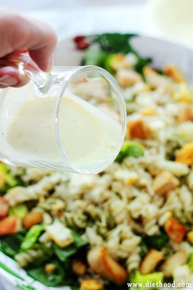 Pouring homemade Light Caesar Dressing over a pasta salad in a bowl.