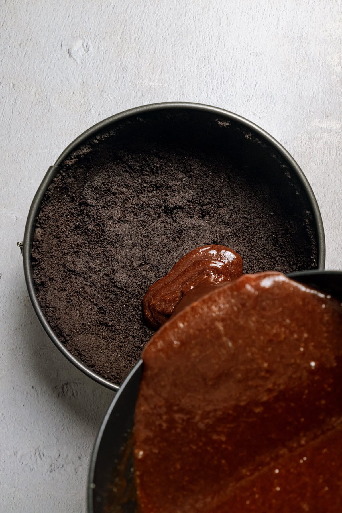 Overhead view of chocolate filling being poured into an Oreo crust in a round cake pan.