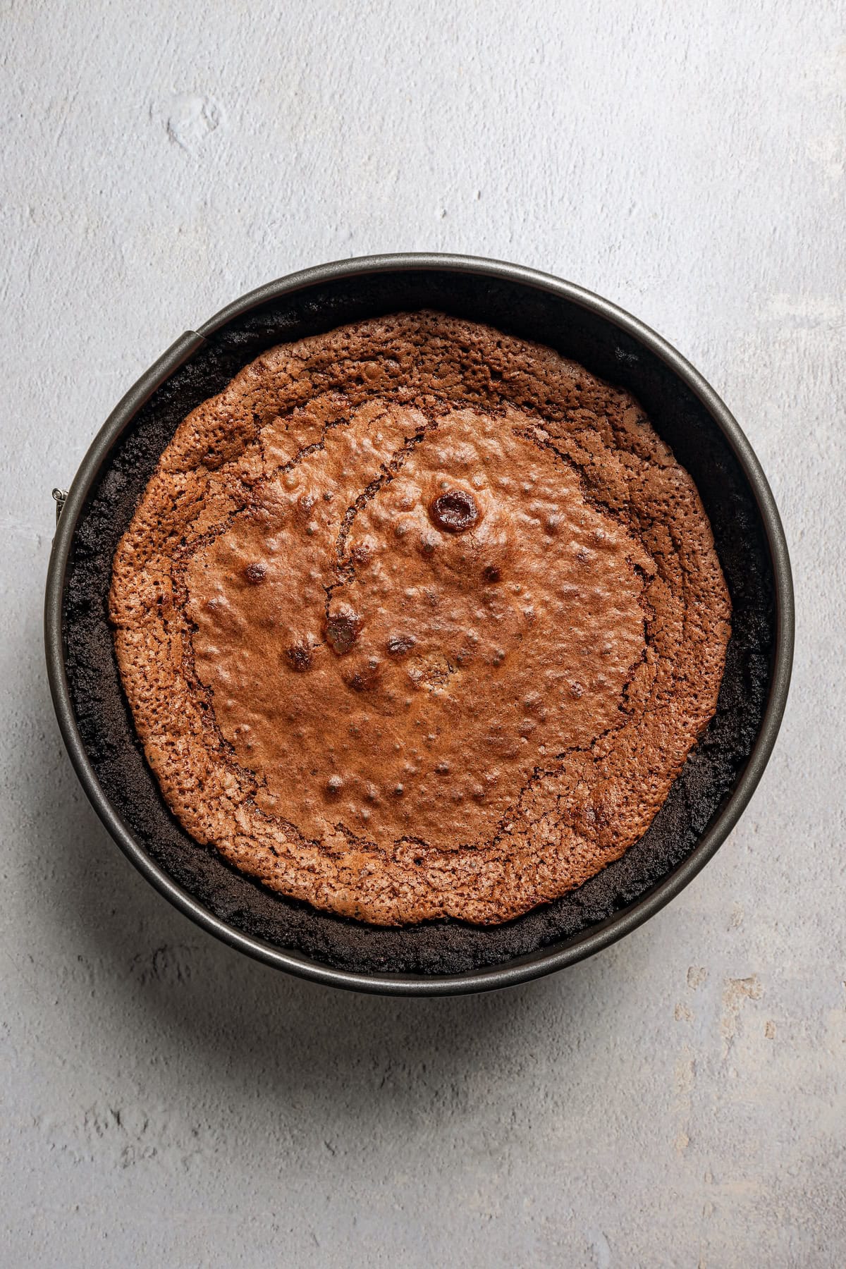 Overhead view of baked chocolate filling inside an Oreo crust in a round cake pan.