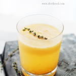 A glass of yellow colored Peach Mimosa topped with thyme