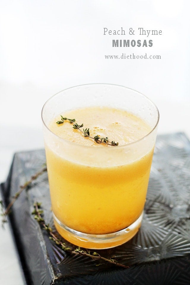 A glass of yellow colored Peach Mimosa topped with thyme