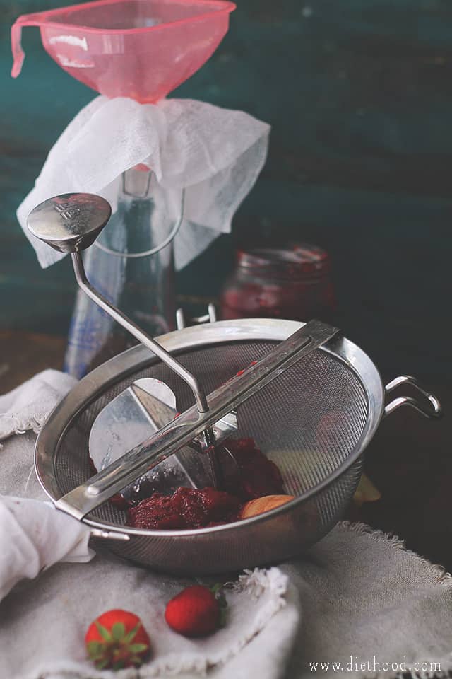 Pressing cooked strawberries through a sieve.