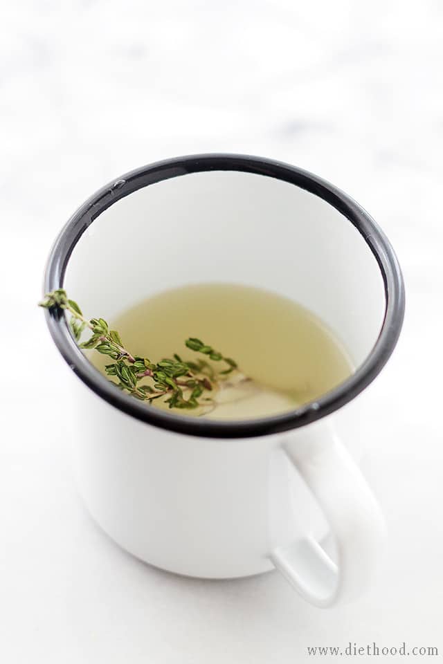 A white mug filled with simple syrup and fresh thyme