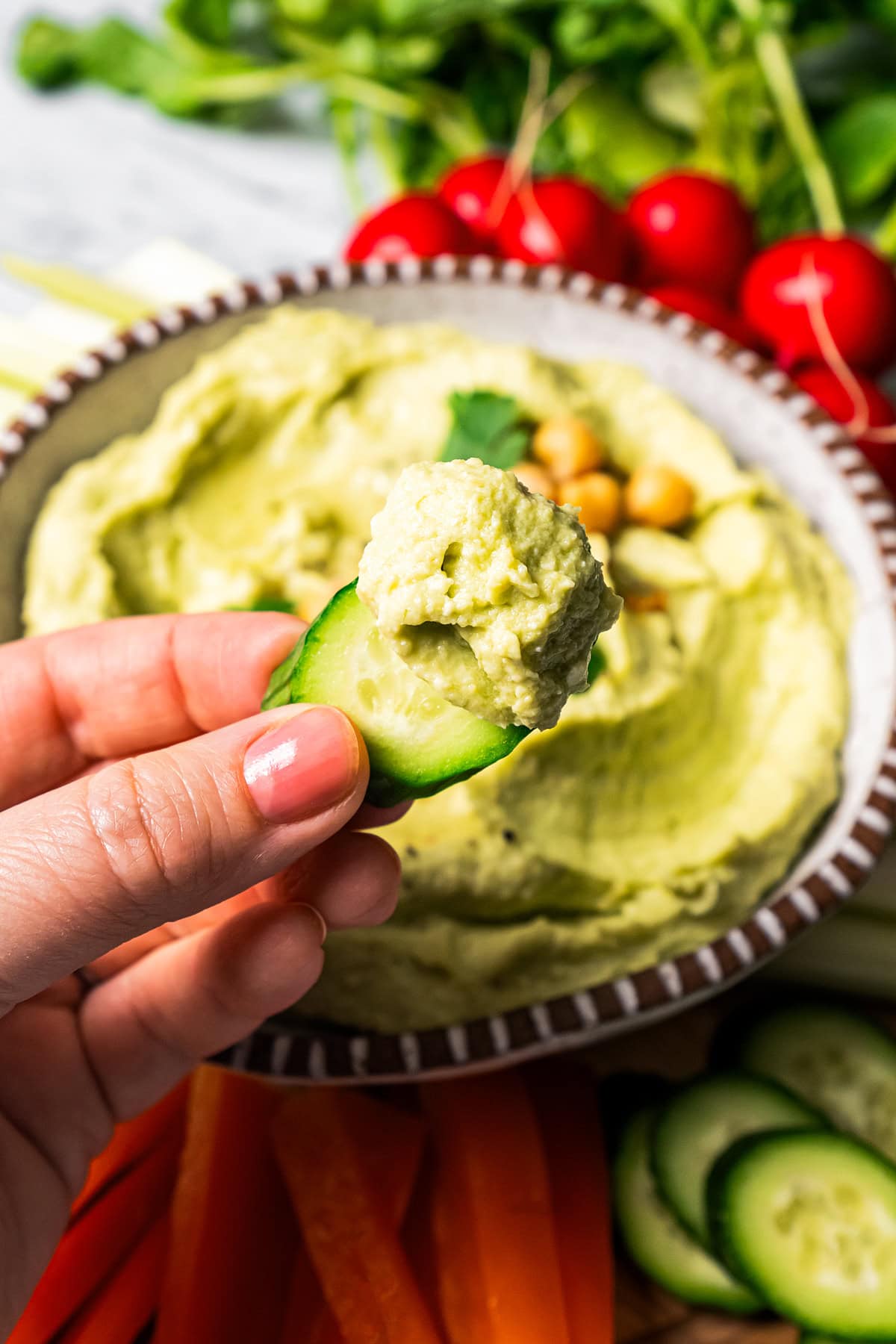 Dipping into a hummus with a slice of cucumber.