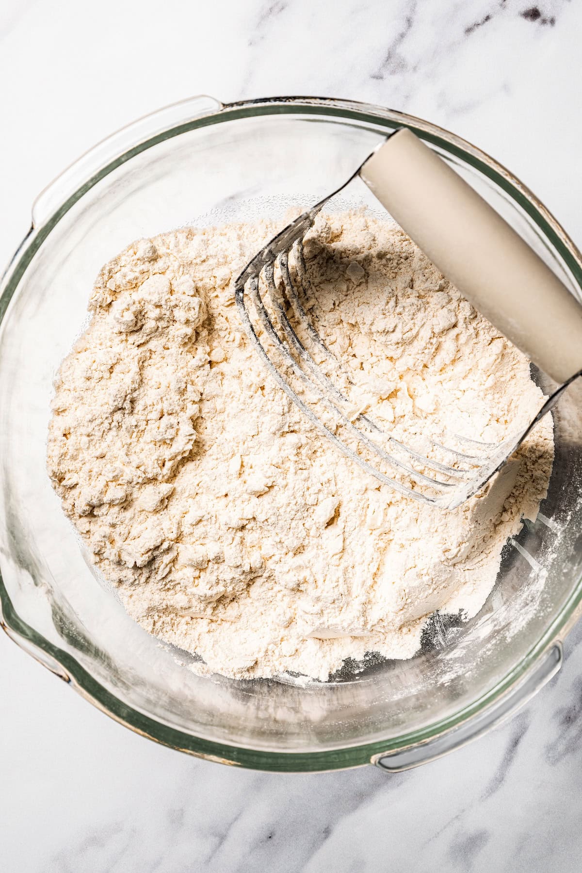 This apple pie cake has juicy caramel apples layered into a buttery crust, baked beneath a soft, sweet cake layer. It's easier than pie! A pastry cutter resting in a bowl of flour cut together with butter.
