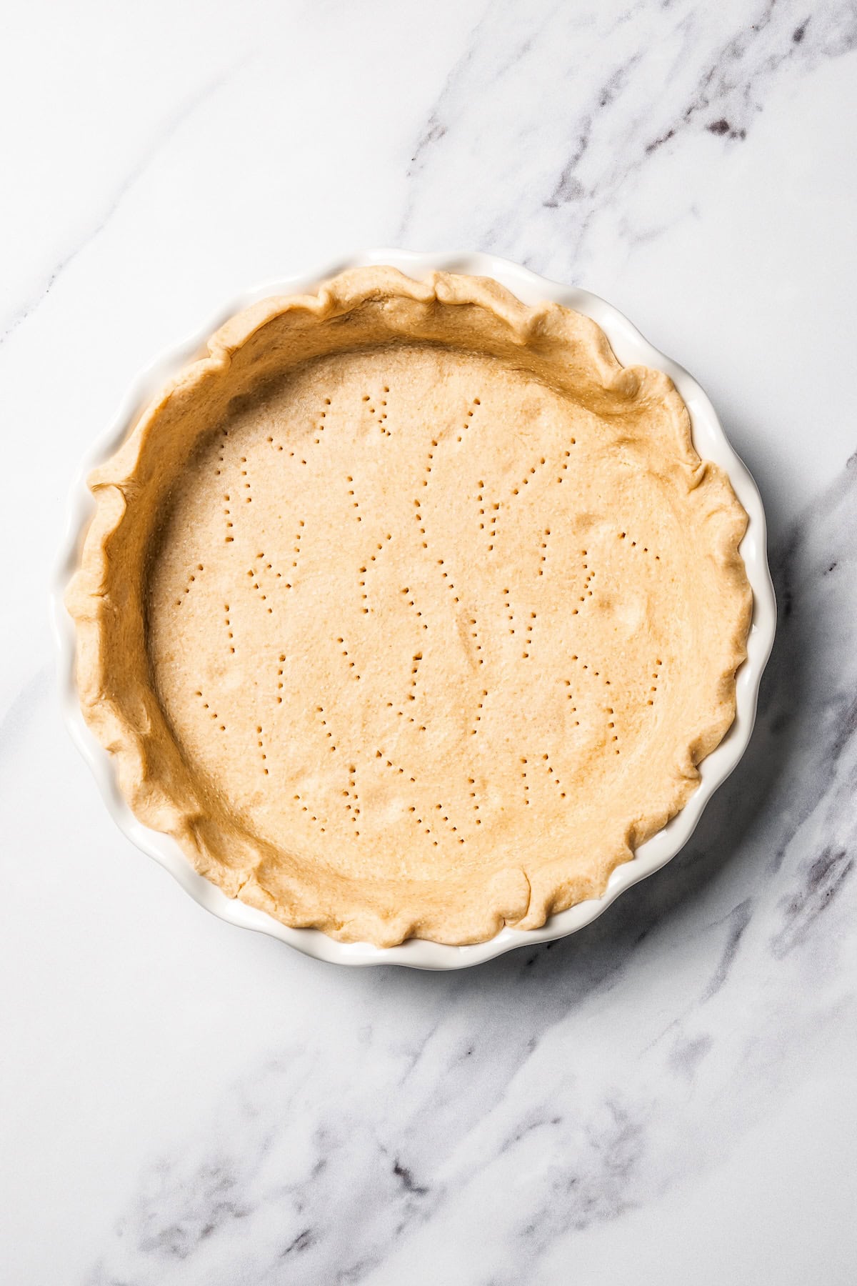 This apple pie cake has juicy caramel apples layered into a buttery crust, baked beneath a soft, sweet cake layer. It's easier than pie! A docked pie crust pricked with a fork inside a deep dish pie plate.