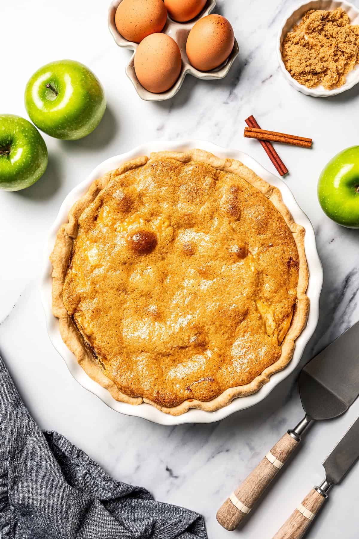 This apple pie cake has juicy caramel apples layered into a buttery crust, baked beneath a soft, sweet cake layer. It's easier than pie! Overhead view of a baked apple pie cake surrounded by ingredients.