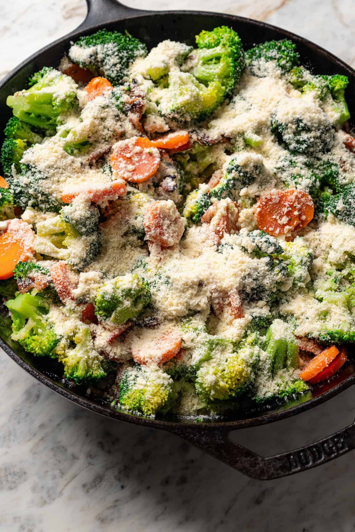 Broccoli and cheese sauce in a skillet with carrots and bacon.