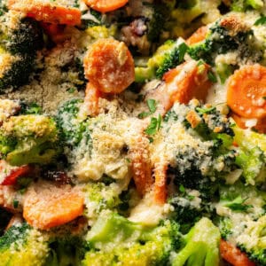 Close up of broccoli and cheese in a skillet with carrots and bacon.