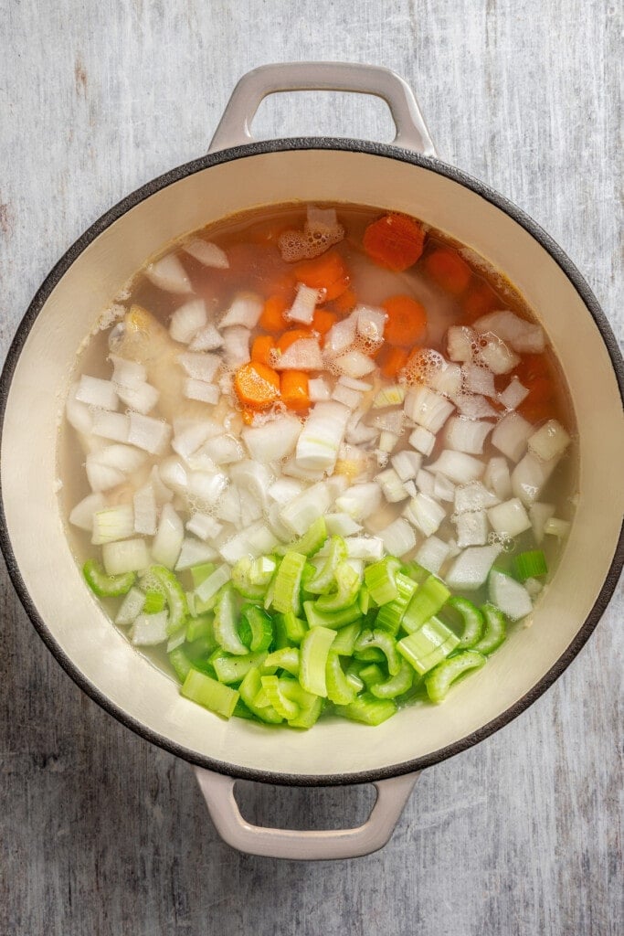 Chopped carrots, onions, and celery added to a pot with chicken drumsticks in water.
