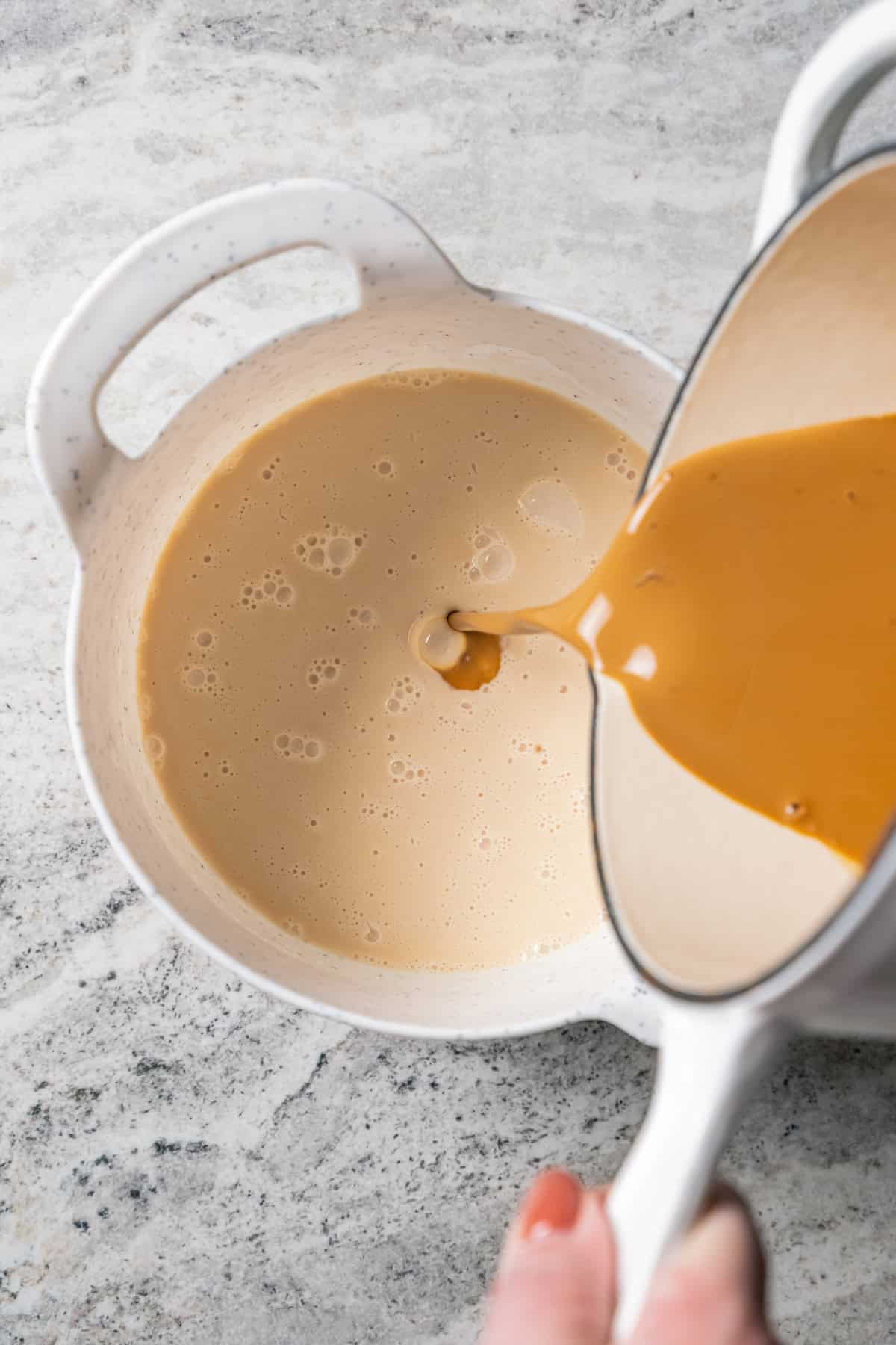 Caramel being poured into coffee cream in a white bowl.