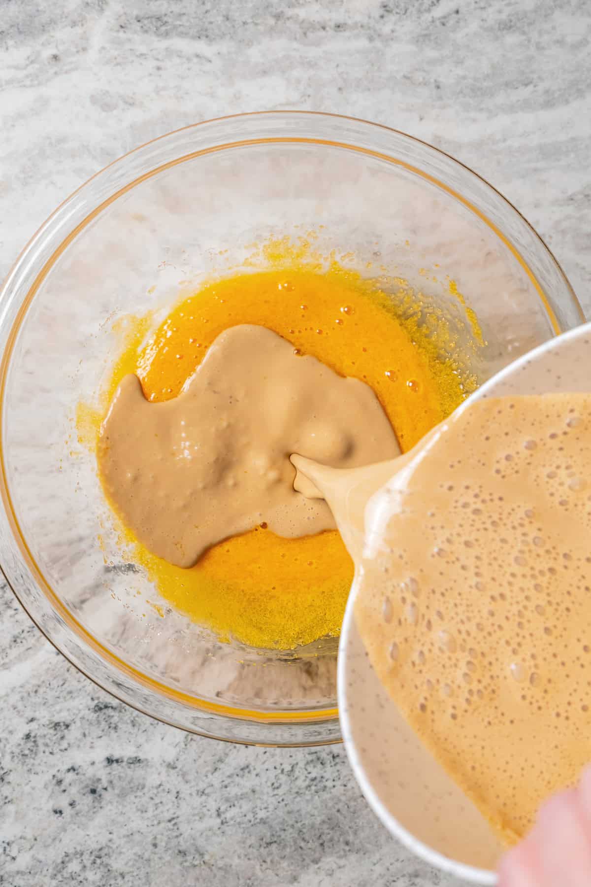 Coffee caramel mixture being poured into the egg yolks and sugar in a bowl.