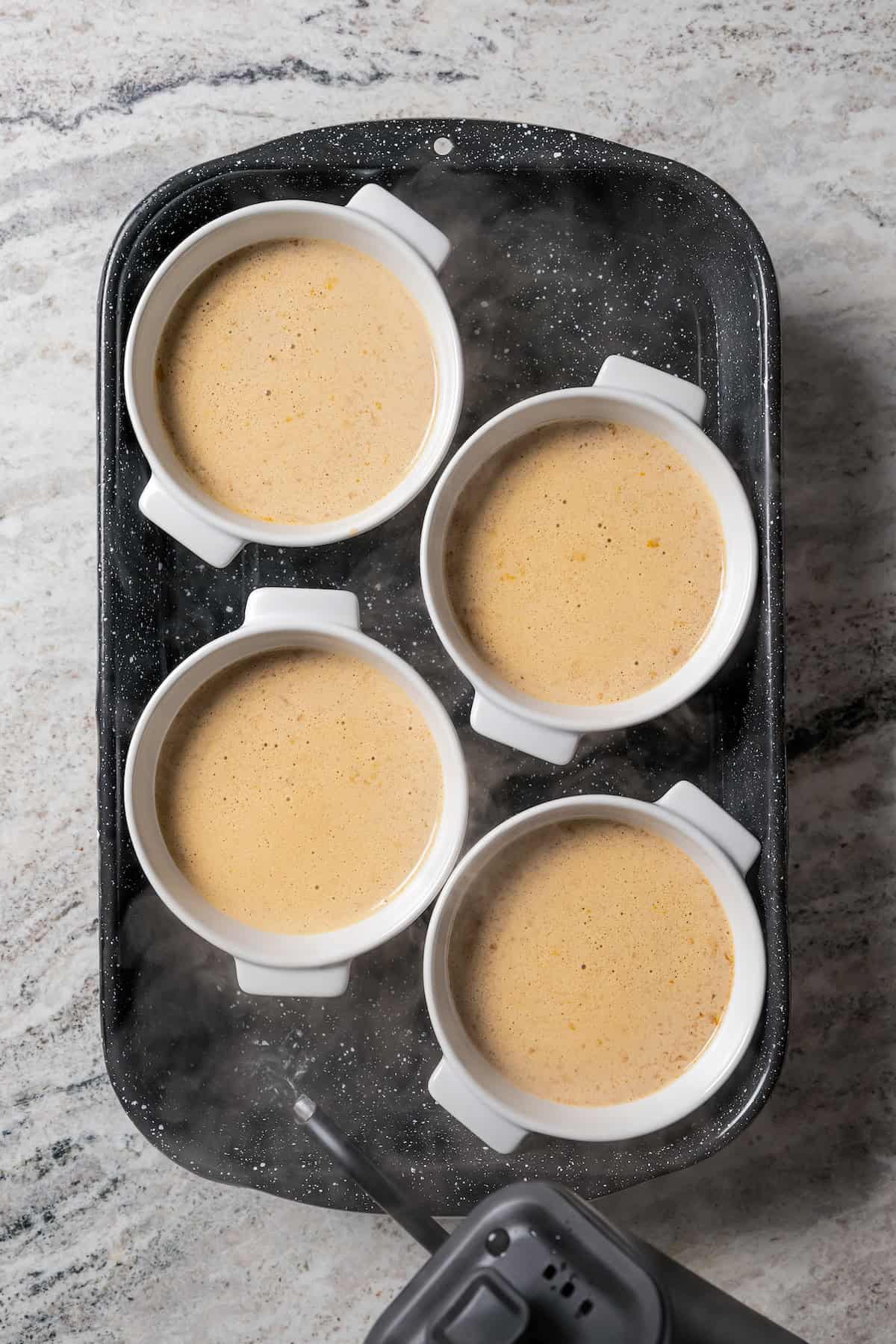 Ramekins filled with coffee crème brûlée batter on a baking sheet.