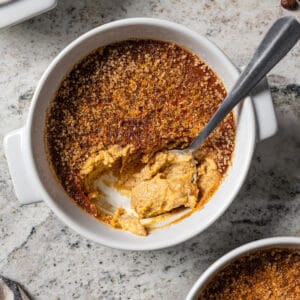 Overhead close up view of a spoon resting in a ramekin of coffee crème brûlée.