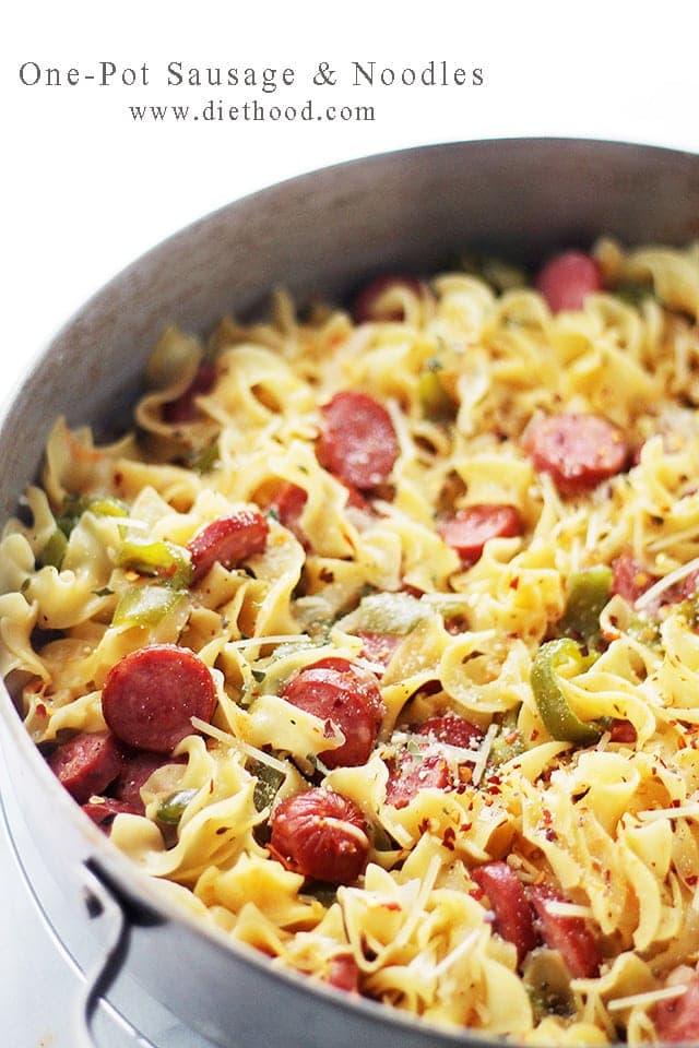 Noodles with smoked sausage slices cooking in a skillet.