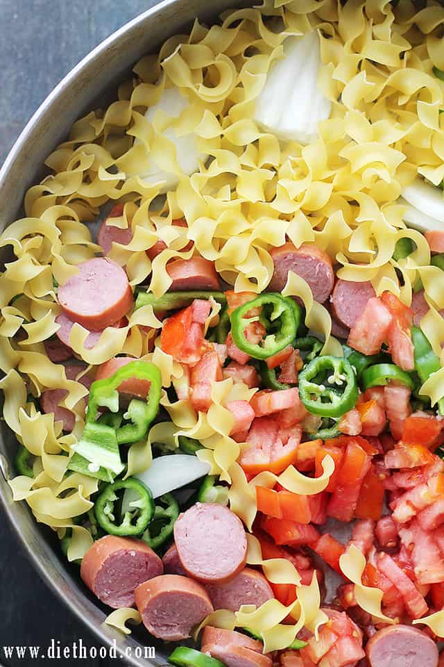 Cooking smoked turkey sausage, noodles, and fresh vegetables in a large skillet.