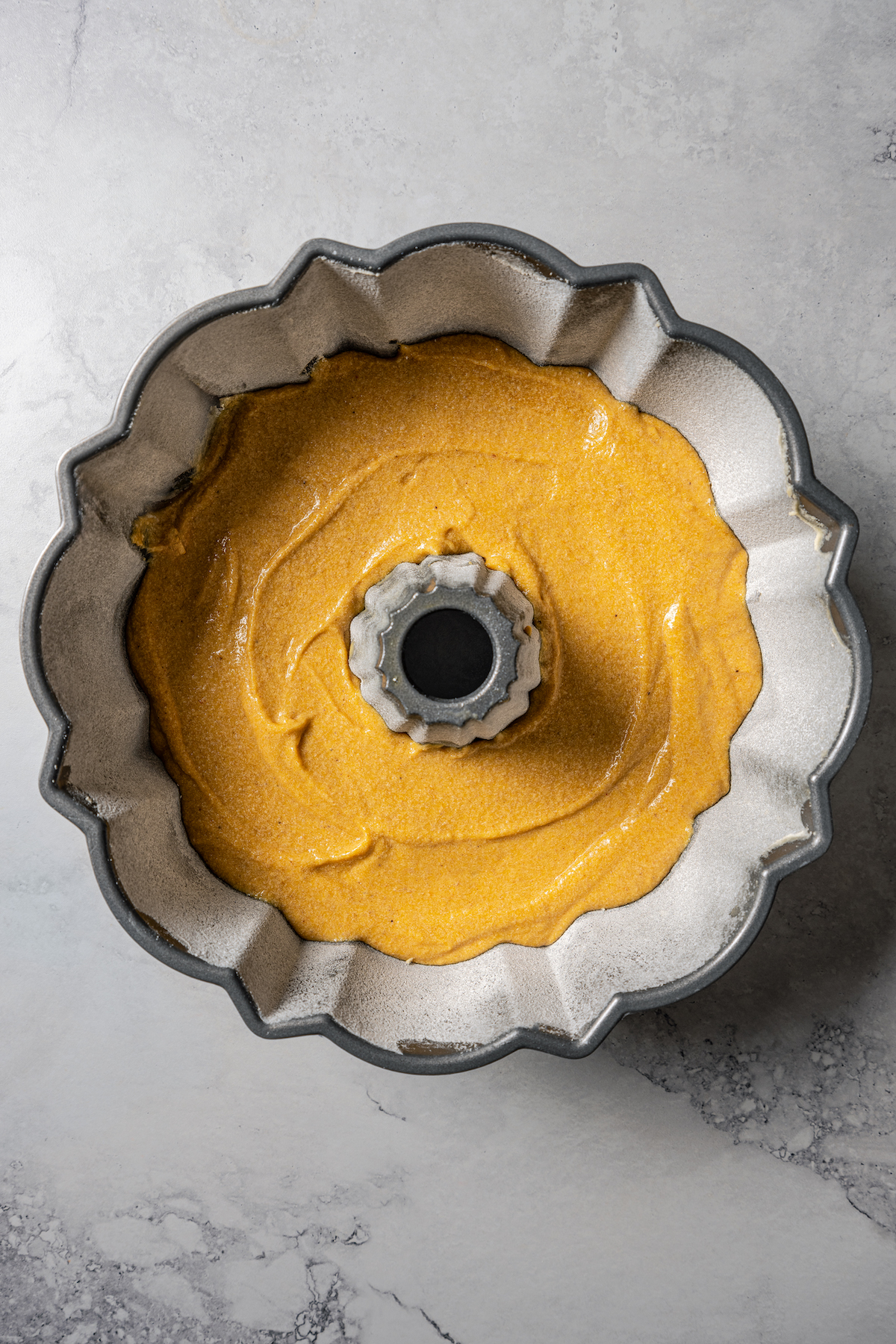 Pumpkin spice cake batter inside a greased and floured bundt pan.