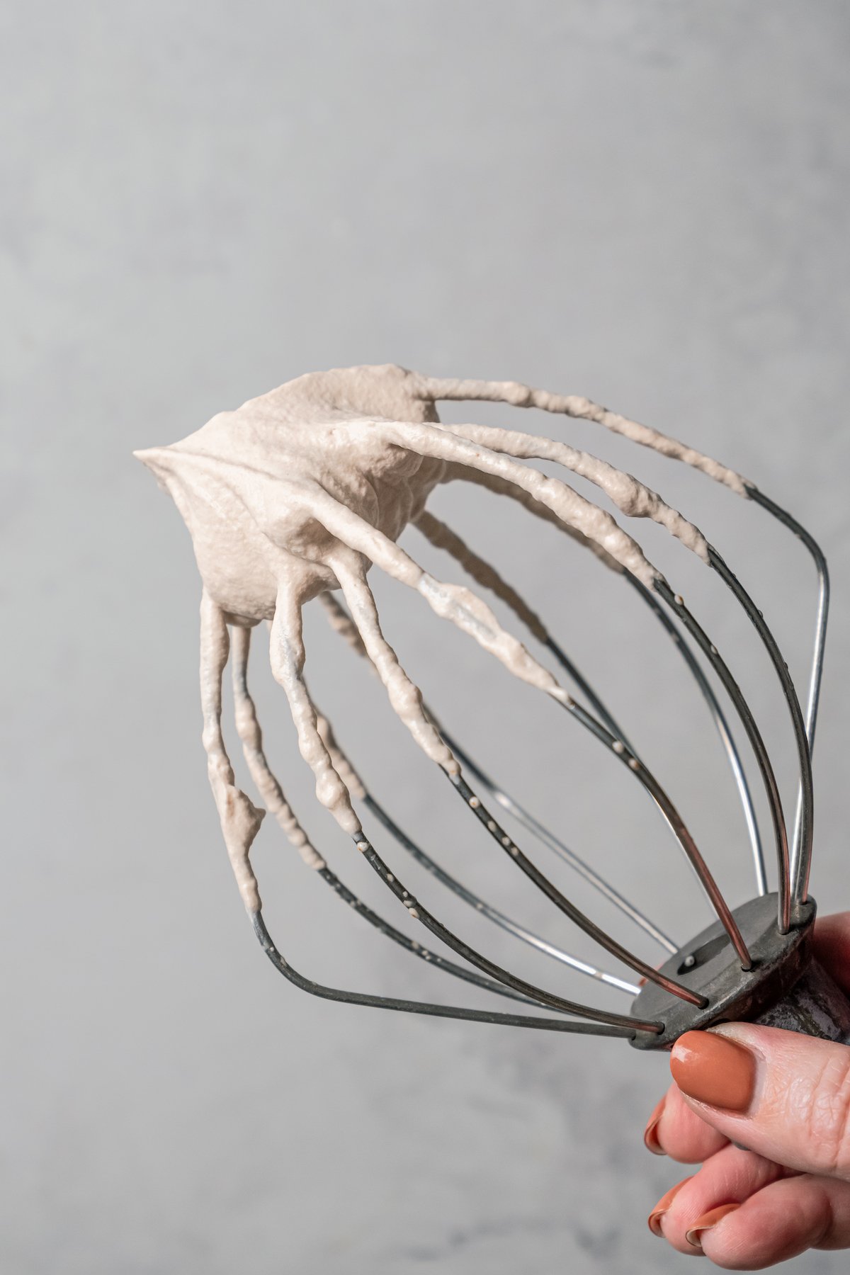 Close up of a hand holding up a whisk attachment covered with espresso whipped cream.