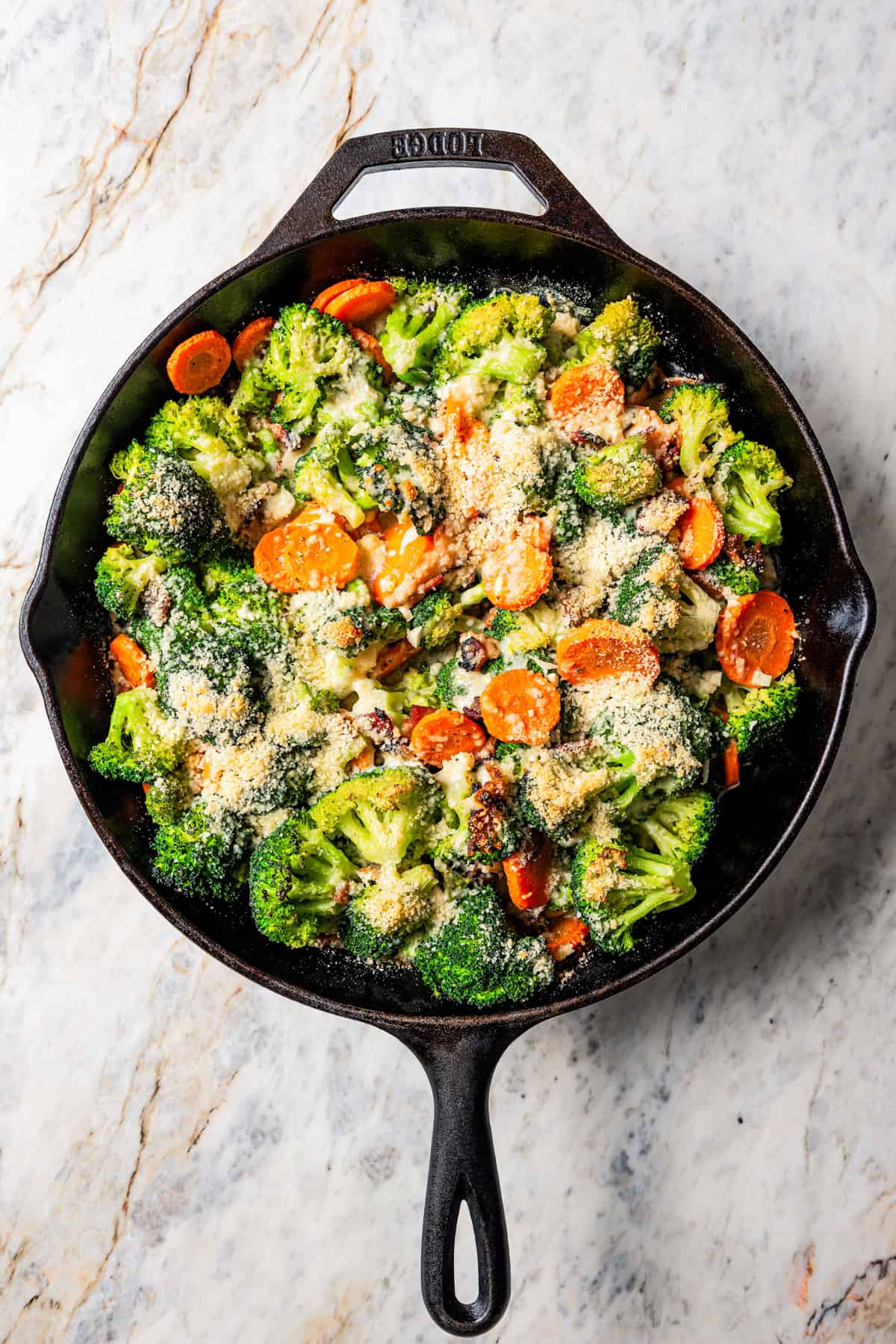 Overhead view of broccoli and cheese in a skillet with carrots and bacon.