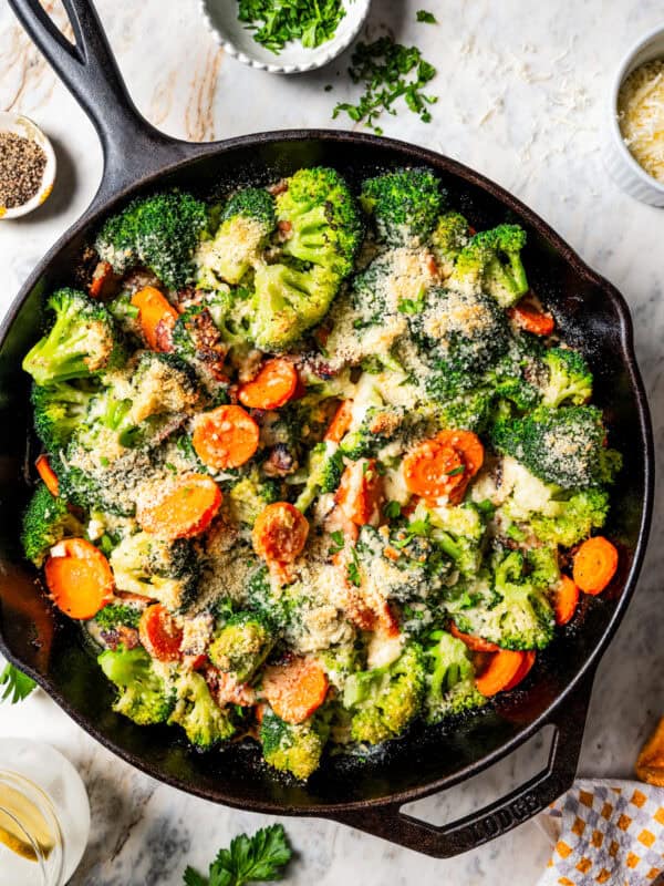 Cooked broccoli and cheese in a skillet with carrots and bacon.