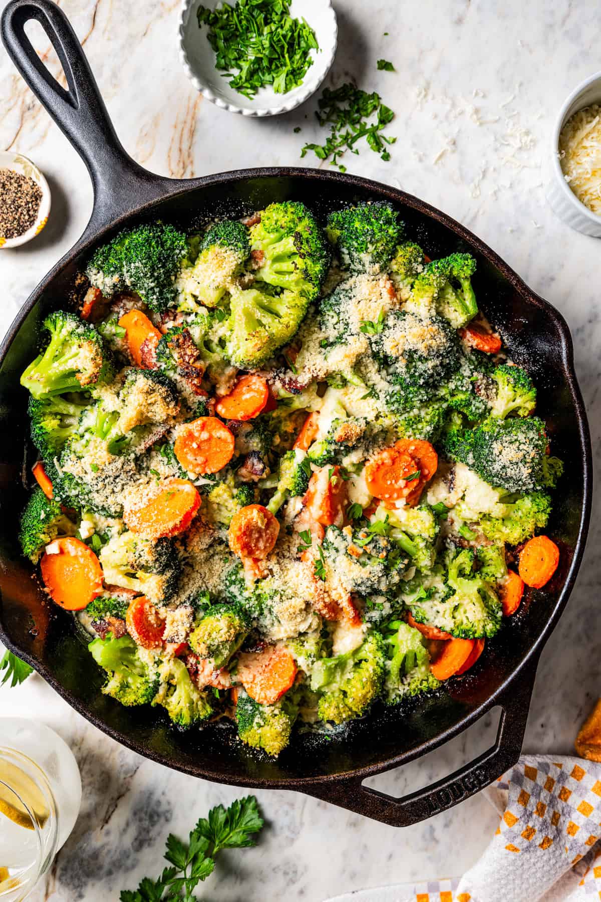 Cooked broccoli and cheese in a skillet with carrots and bacon.