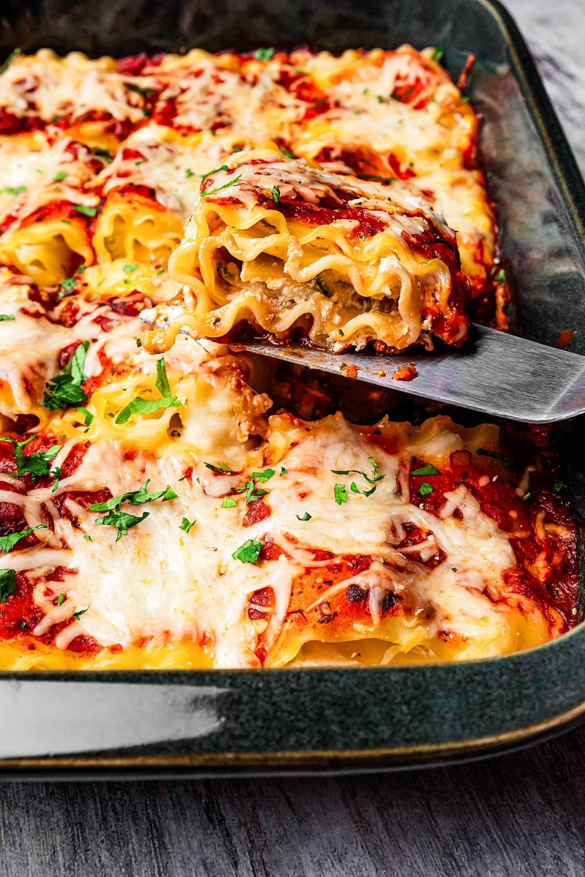 A spatula lifting a lasagna roll from a baking pan.