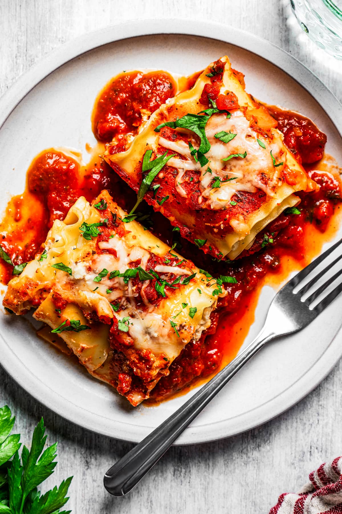 Overhead close-up view of two lasagna roll ups served on a white plate next to a fork.