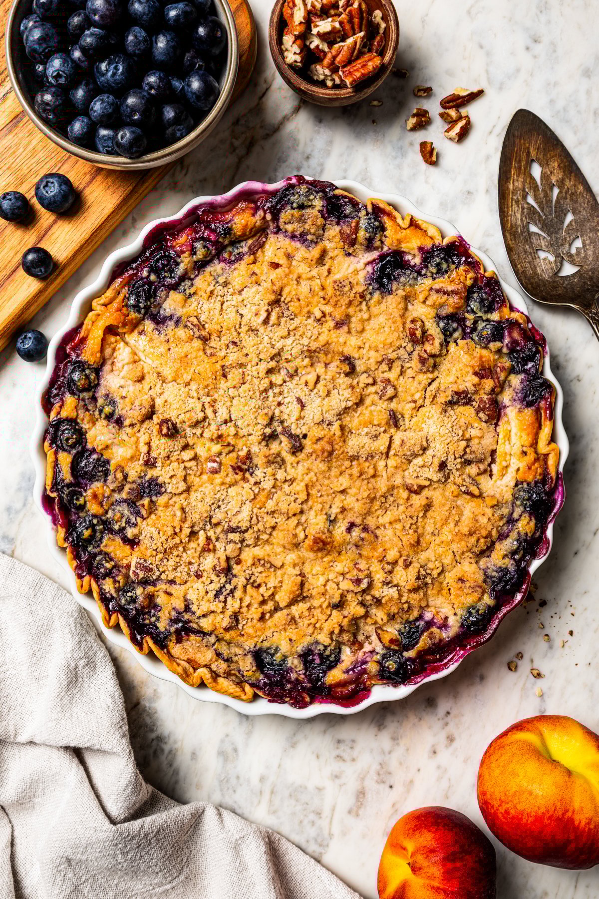 This peach blueberry pie is a fruit-filled custard pie bursting with juicy fresh peaches and blueberries, topped with a nutty pecan streusel. Overhead view of a whole peach blueberry pie topped with streusel.