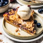 A slice of peach blueberry pie topped with a scoop of vanilla ice cream on a plate.