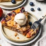 A fork resting on the end of a slice of peach blueberry pie, topped with a scoop of vanilla ice cream on a plate. photo by diethood.com