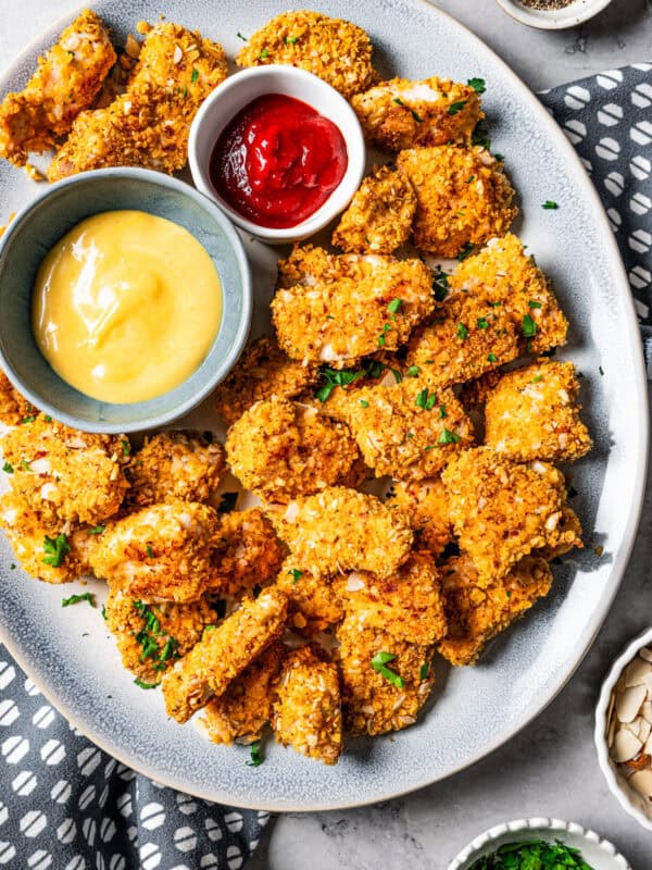 Overhead view of pecan crusted chicken on a platter with two small bowls of dipping sauces.