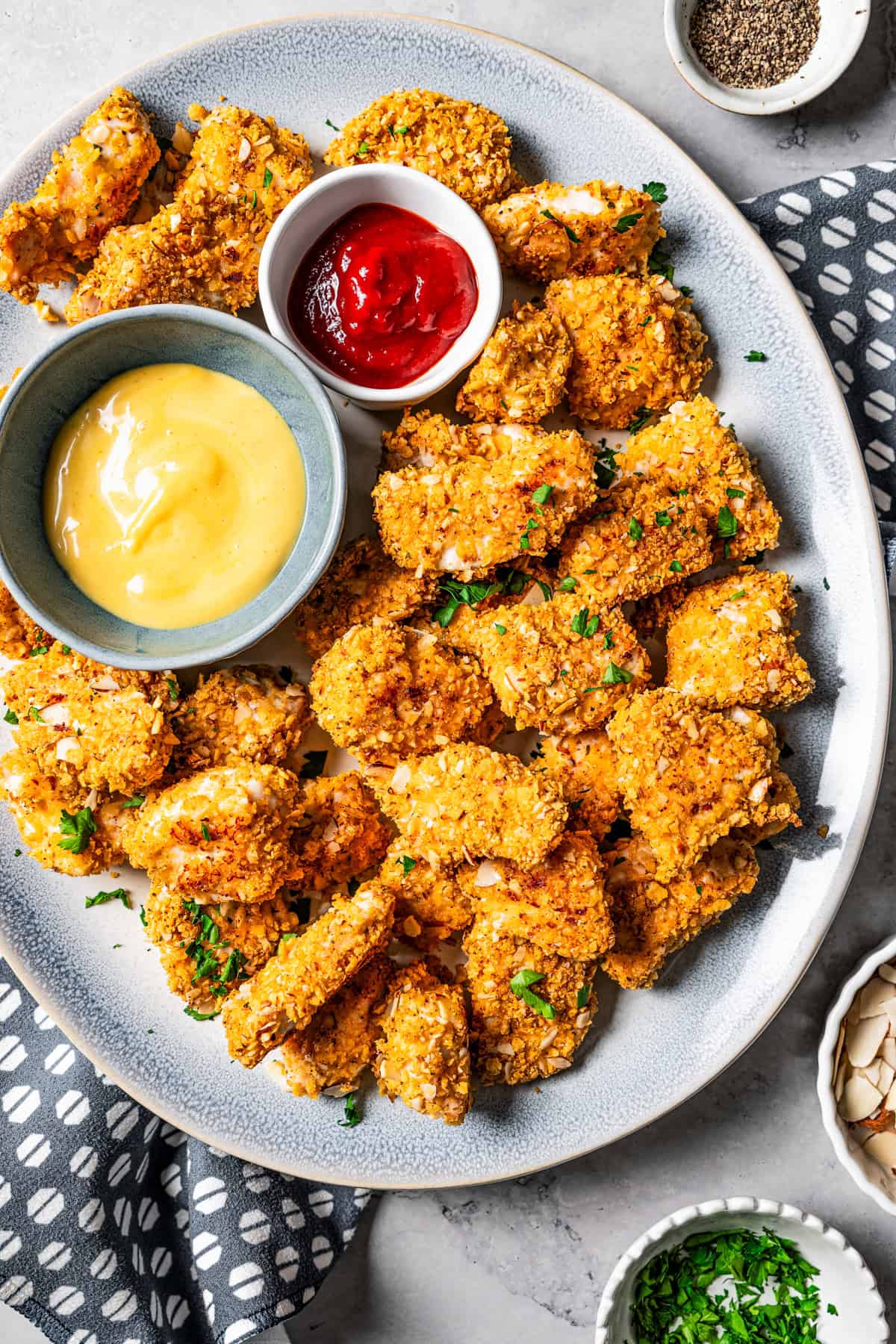 Overhead view of pecan crusted chicken on a platter with two small bowls of dipping sauces.