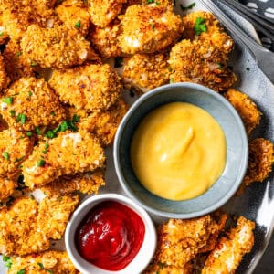 A plate of chicken nuggets with a small bowl of ketchup and a bowl of mustard set in the center of the plate.