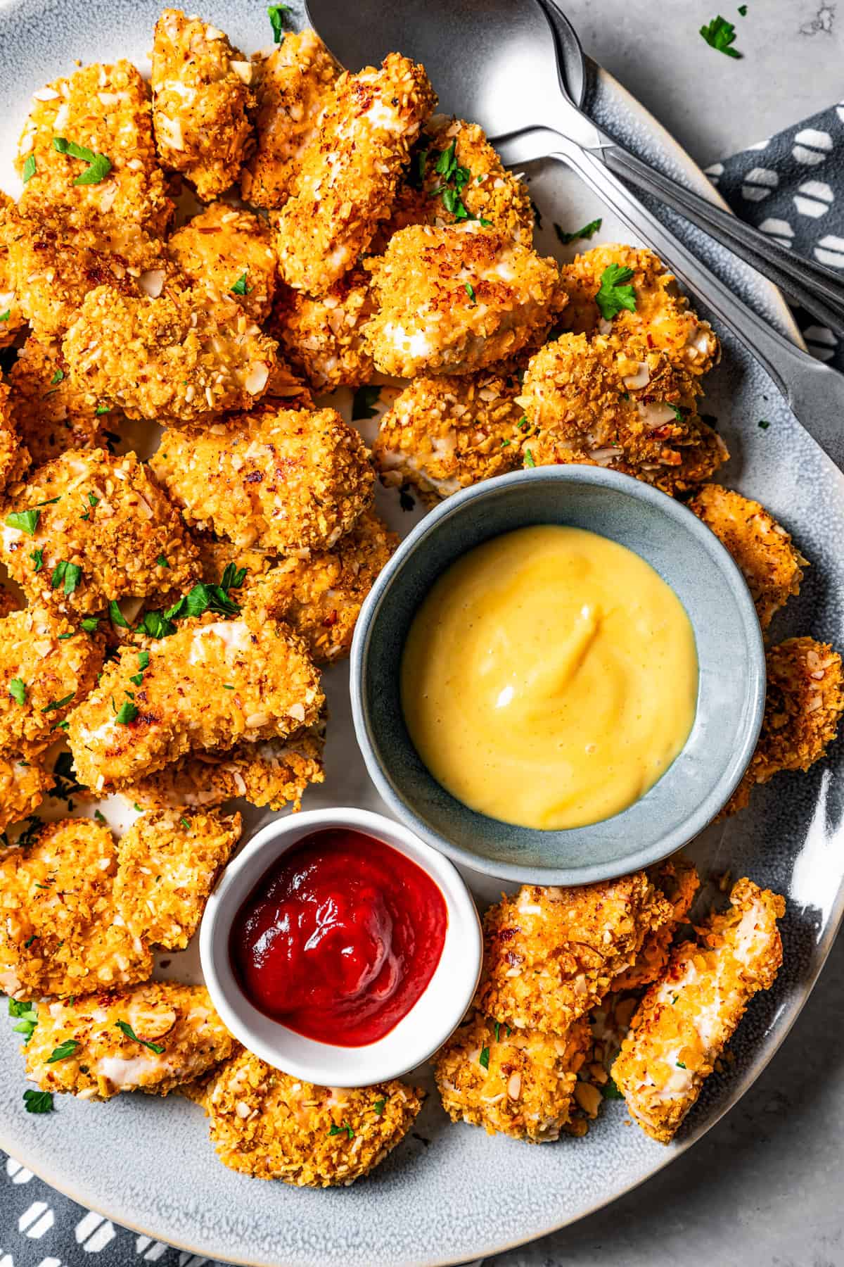 A plate of chicken nuggets with a small bowl of ketchup and a bowl of mustard set in the center of the plate.