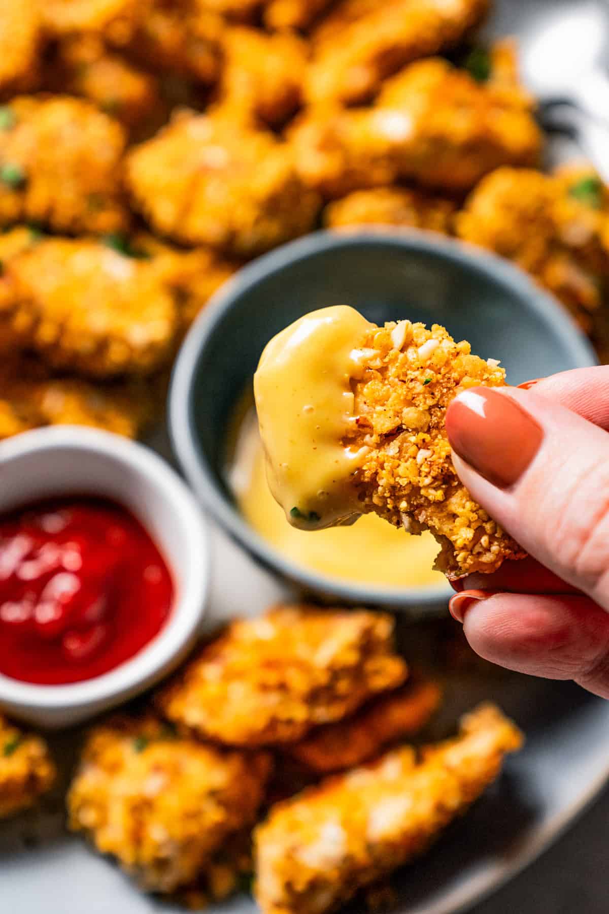 A hand holding up a chicken nugget that was dipped in mustard.